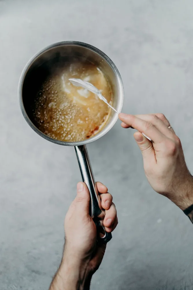 A person stirring hot caramel sauce in a saucepan, creating delicious dessert topping.
