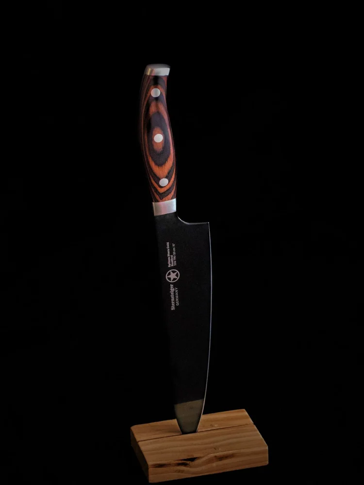 A sharp chef's knife displayed vertically against a black background.