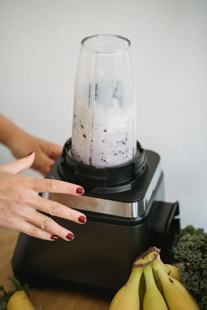 Close-up of hands using blender with bananas and greens for smoothie.