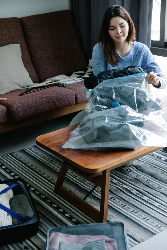 Young woman organizing clothes in vacuum bags, preparing for travel in a comfortable living room setting.