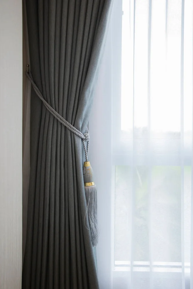 Soft gray curtain with decorative tassel tieback complemented by sheer white curtain