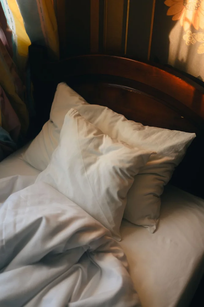 Sunlit unmade bed with plush pillows and soft linens, creating a cozy and inviting ambiance.