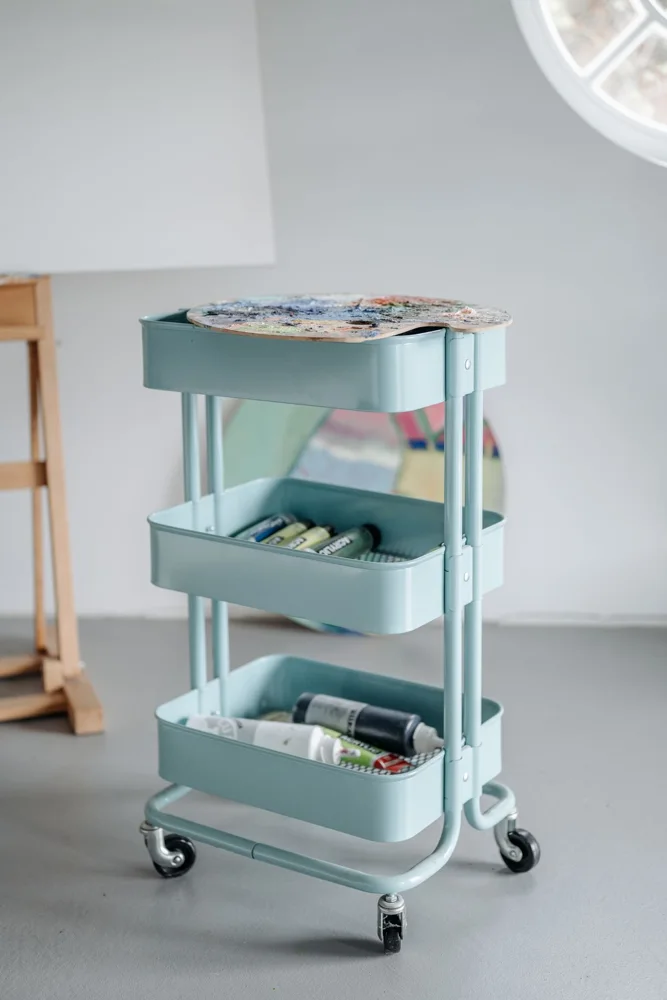Organized art supplies in a mobile cart within an artistic studio setting.