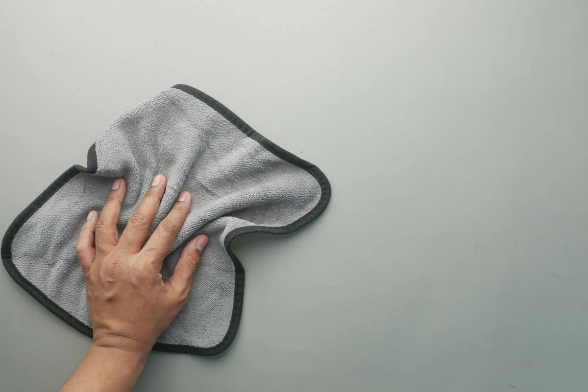 A hand wipes a light-colored table using a gray microfiber cloth, ideal for cleaning concepts.