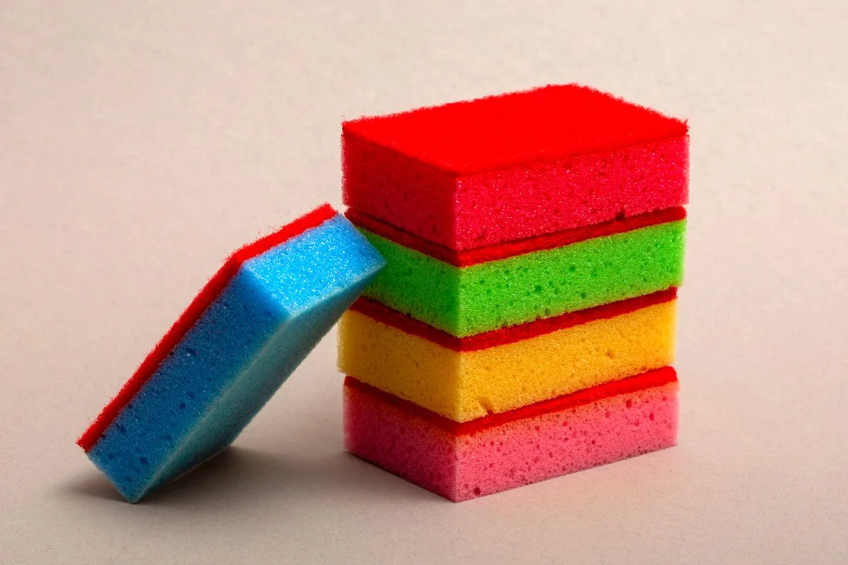 Stack of colorful kitchen sponges showing vibrant red, green, yellow, and blue hues in a studio setting.