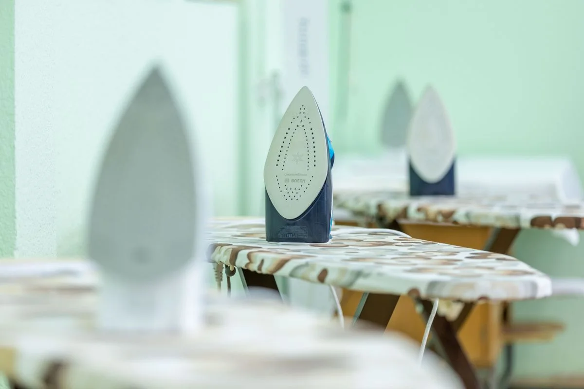 Close-up of modern irons placed on ironing boards with camouflage pattern covers in a bright indoor setting.