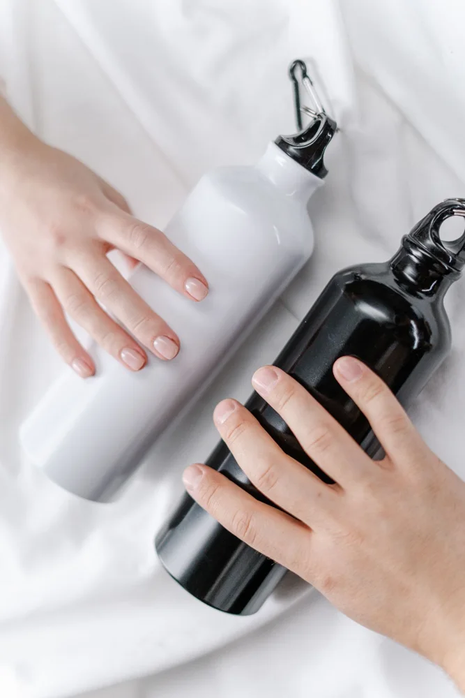 Close-up of hands holding black and white insulated water bottles on a soft white background.
