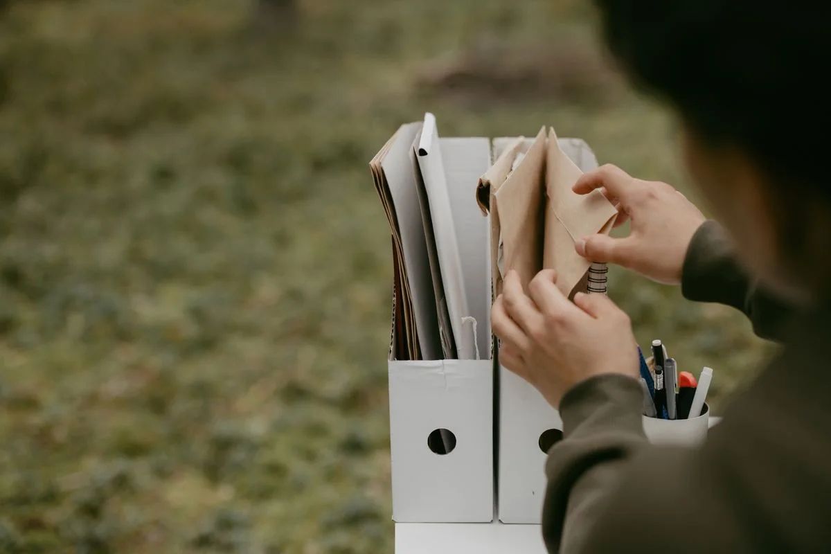Person sorting documents in folders outdoors, hands visible, neutral tone.