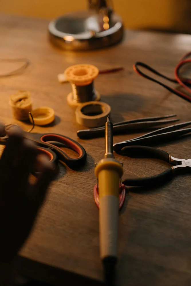 A close-up view of soldering and electronic repair tools on a wooden workbench.