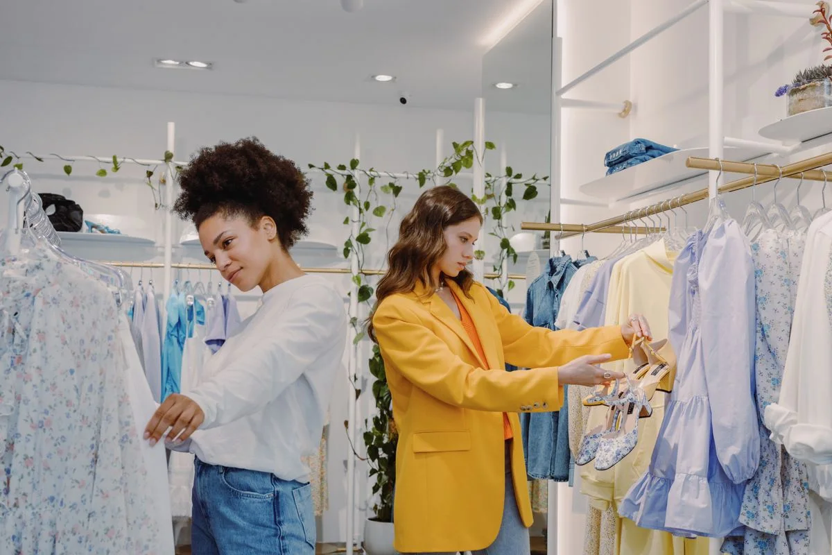 Two women shopping in a trendy clothing store, browsing stylish outfits.