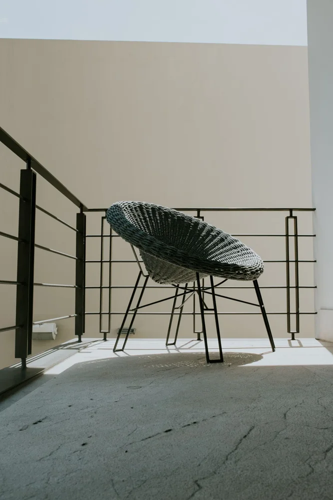 Wicker chair on a minimalist balcony with railings under a clear sky.